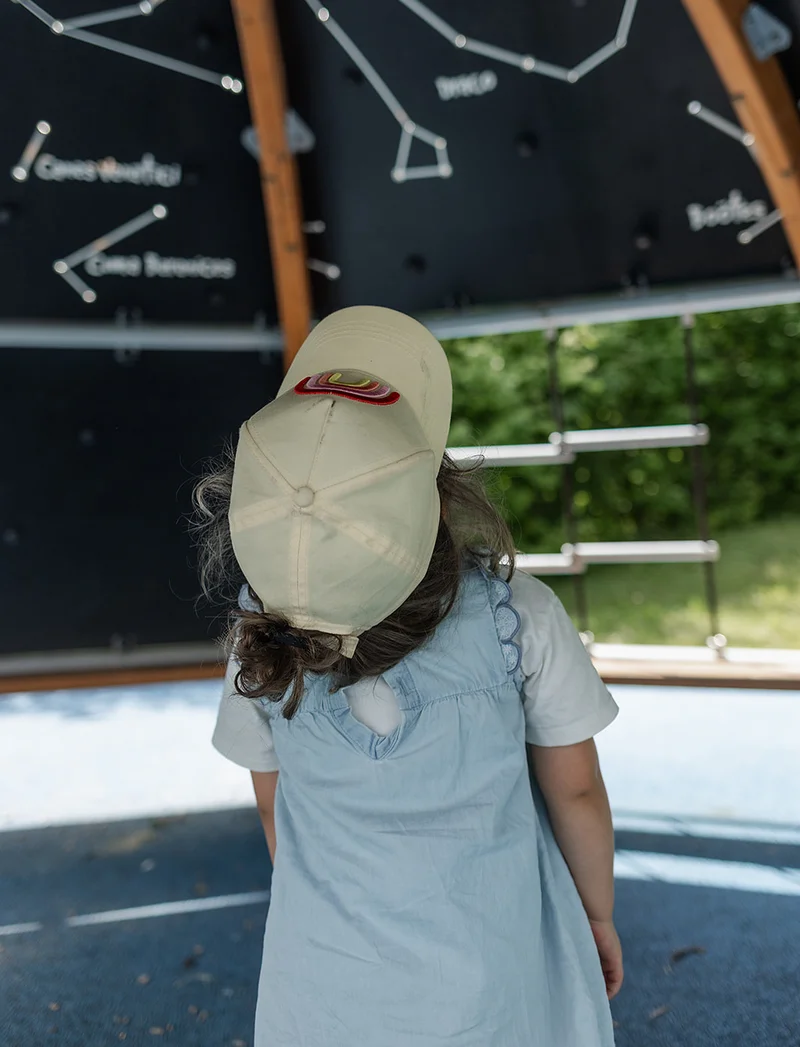 Ein kleines Mädchen mit Basecap blickt in einem überdachten Spielbereich auf eine Wand mit Sternbildern.