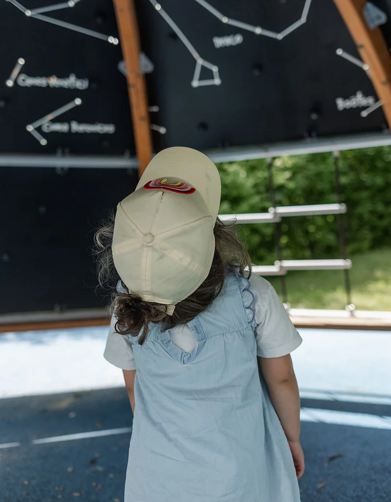 Ein kleines Mädchen mit Basecap blickt in einem überdachten Spielbereich auf eine Wand mit Sternbildern.