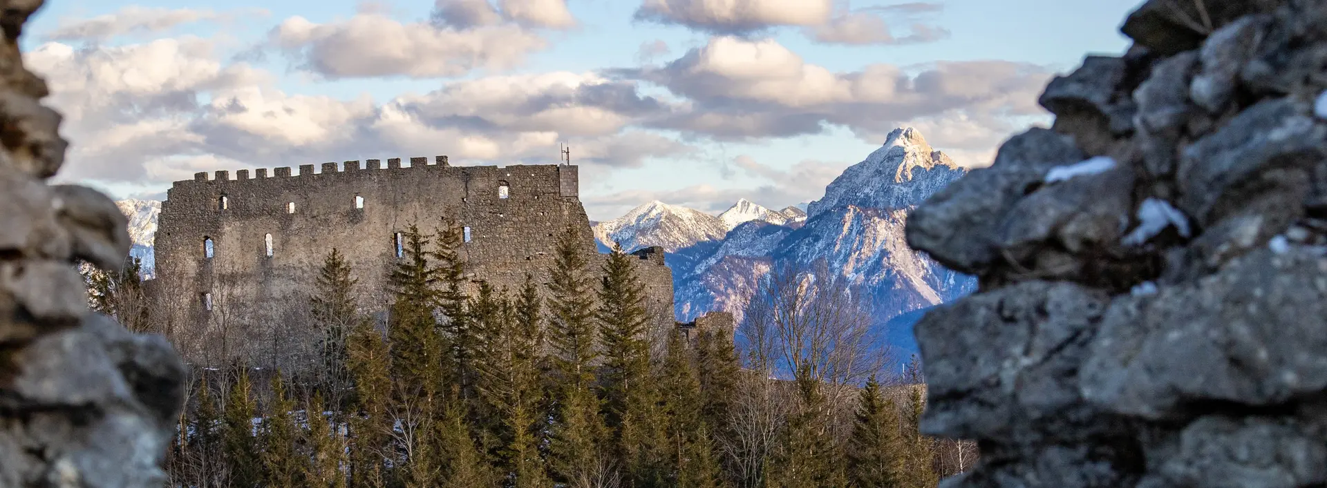 Blick auf die Burgruine Eisenberg in einer tollen Bergkulisse mit weißen Gipfeln.
