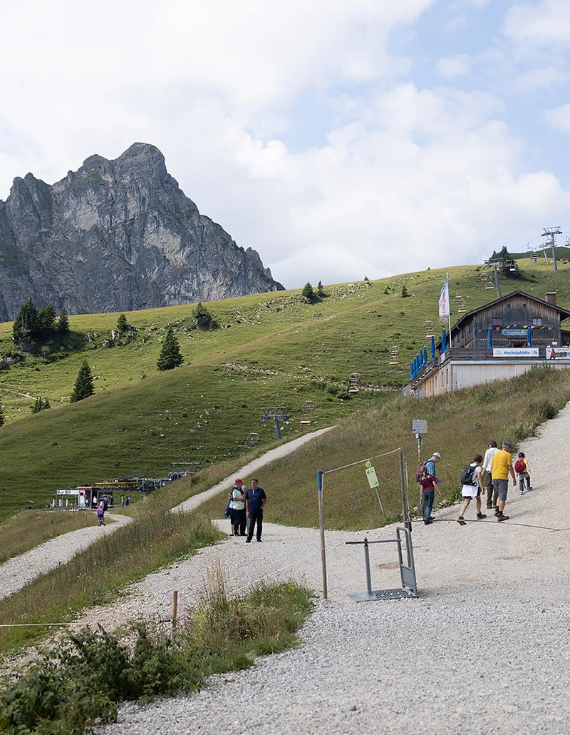 Wanderer auf Bergweg mit der Hochalphütte und der Breitenbergbahn, und einem Berg im Hintergrund.