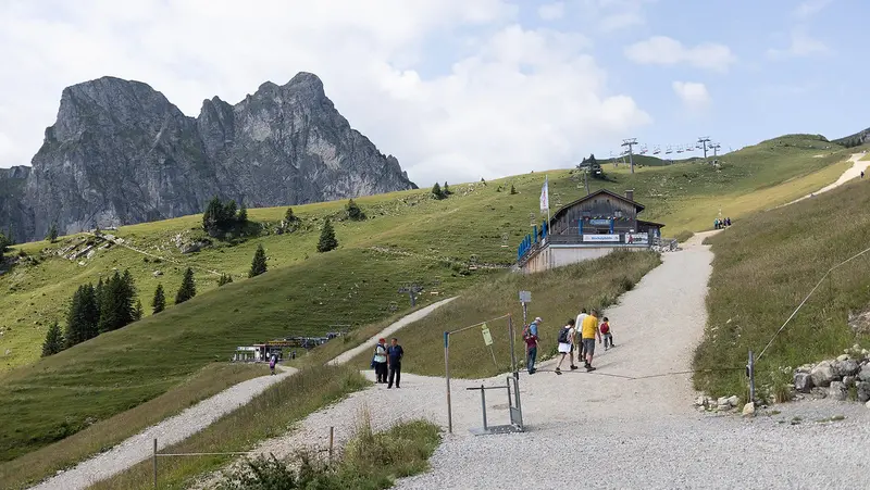Wanderer auf Bergweg mit der Hochalphütte und der Breitenbergbahn, und einem Berg im Hintergrund.