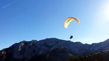 Tandemflug mit dem Gleitschirm am Breitenberg im Allgäu Ein Gleitschirmflieger schwebt vor einer beeindruckenden Bergkulisse.