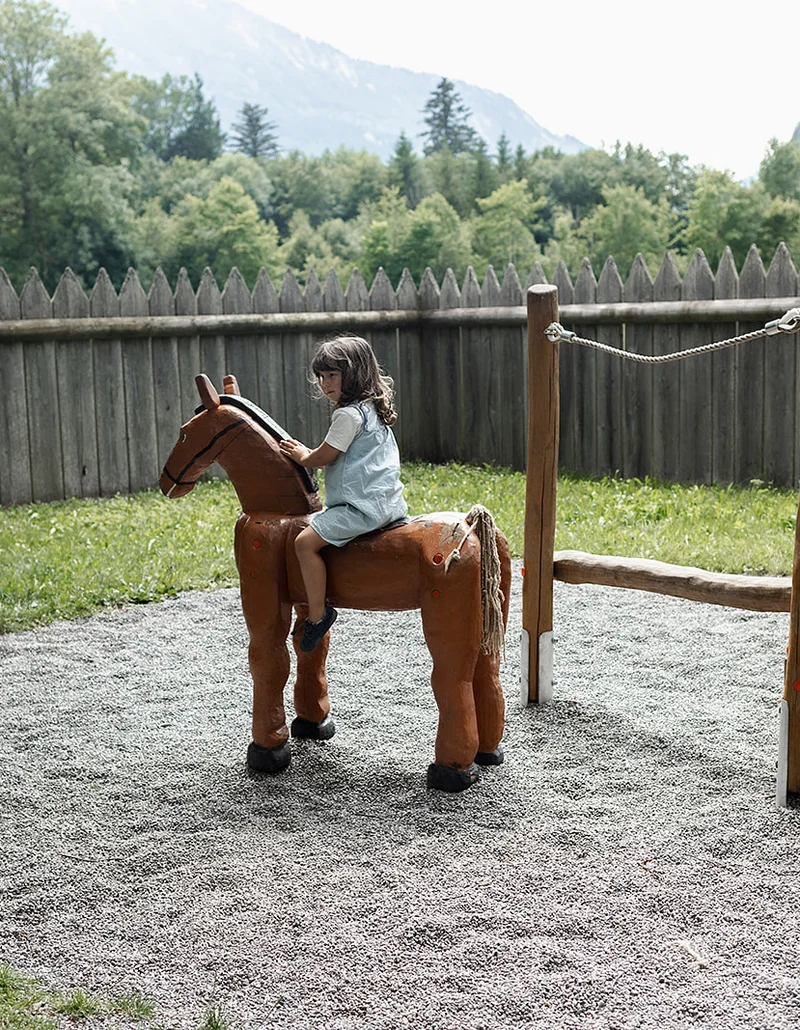 Ein Mädchen sitzt auf einem hölzernen Pferd.