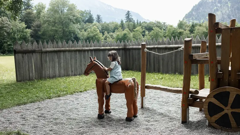 Ein Mädchen sitzt auf einem hölzernen Pferd.