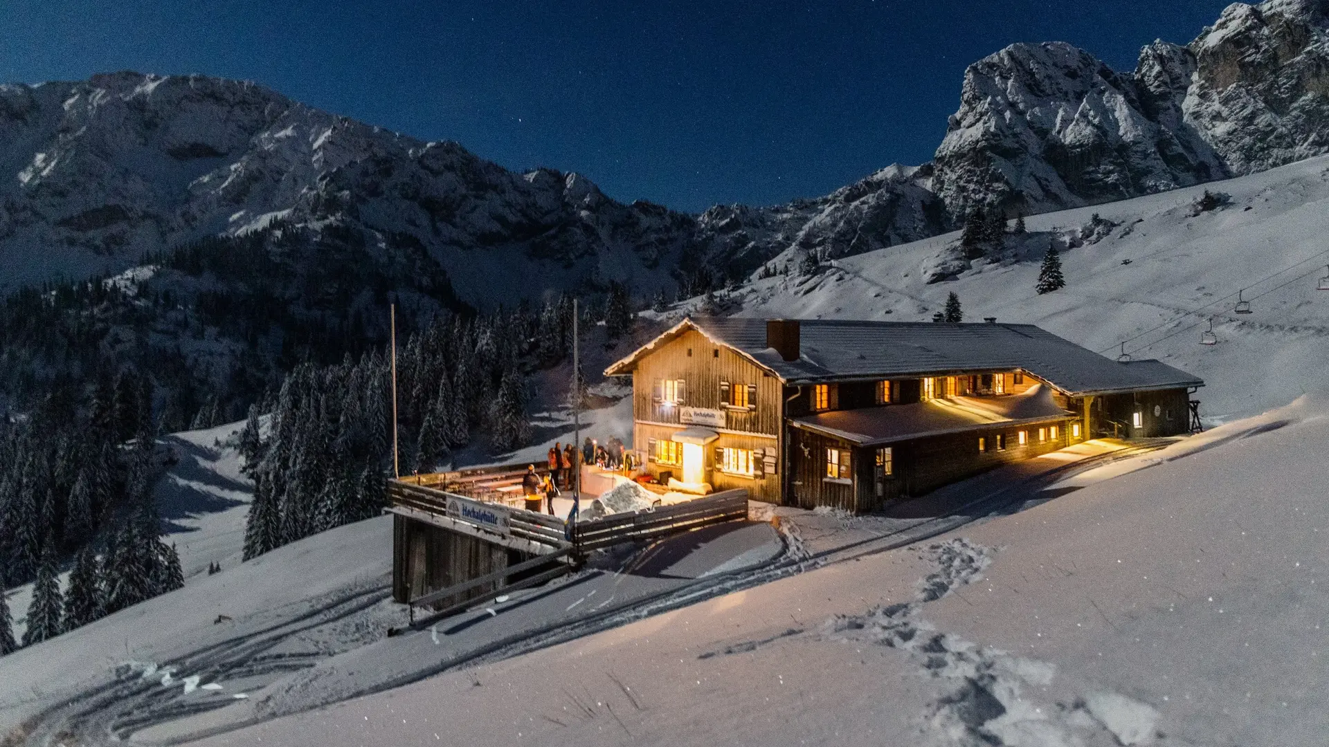 Die Hochalphütte in Pfronten in einer idyllisch verschneiten Landschaft und magischen Beleuchtungen bei Nacht. 