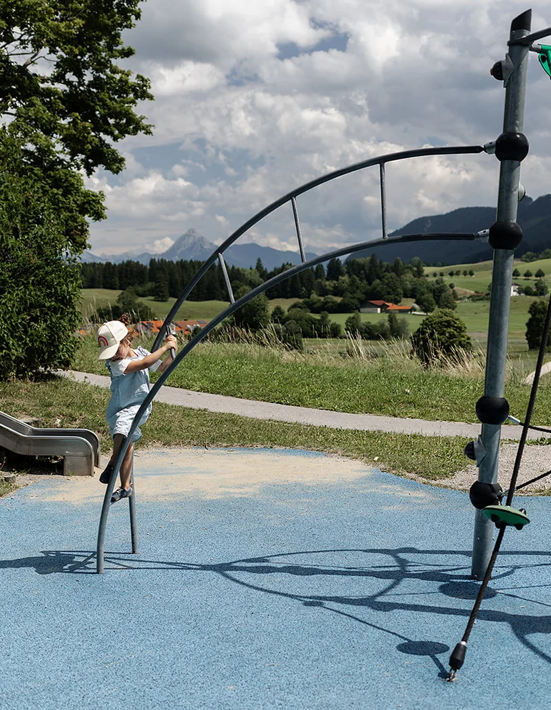 Ein Mädchen spielt auf einem Klettergerüst, im Hintergrund ist eine Hügellandschaft.