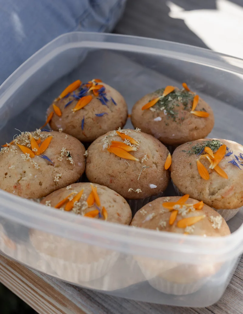 Muffins mit essbaren Blüten in einer Tupperdose.