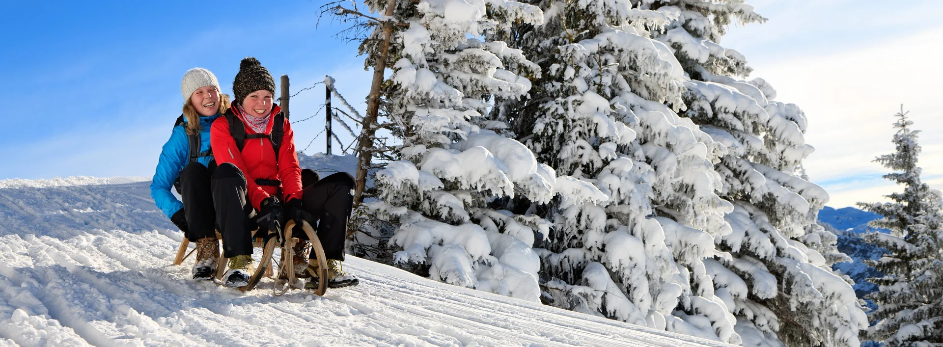 Rodler auf einem winterlichen Hang, im Hintergrund eine idyllisch verschneite Bergkulisse.