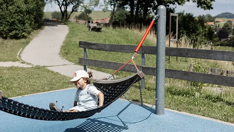 Ein Mädchen sitzt auf einer Hängematte auf dem Spielplatz.