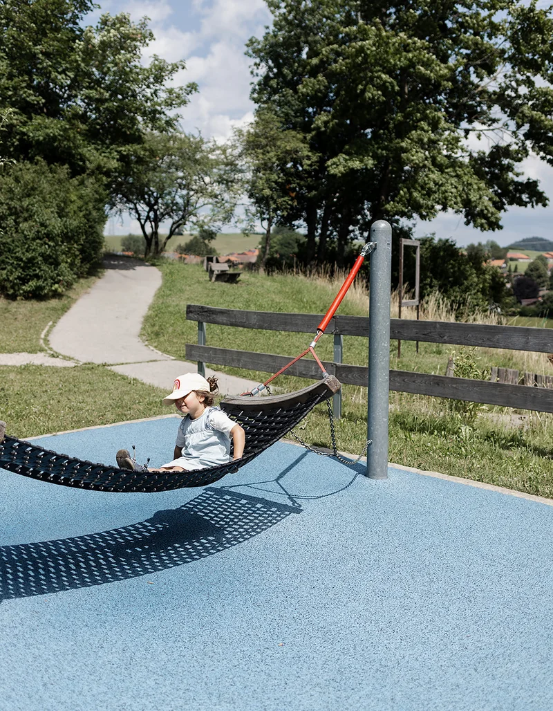 Ein Mädchen sitzt auf einer Hängematte auf dem Spielplatz.
