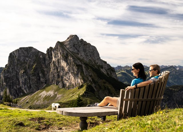 Zwei Wanderer auf einer Sitzbank mit Blick auf die beeindruckende Bergkulisse.