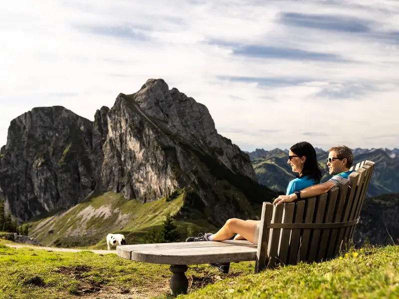 Zwei Wanderer auf einer Sitzbank mit Blick auf die beeindruckende Bergkulisse.