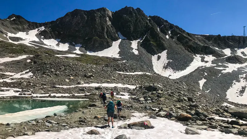 Eine Gruppe Wanderer in einer rauen Berglandschaft, die teilweise noch mit Schnee bedeckt ist.