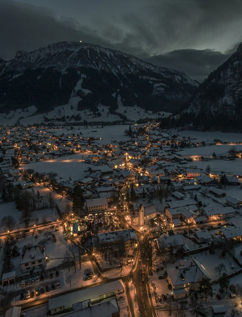 Blick von oben auf das verschneite und schön beleuchtete Pfronten bei Nacht.