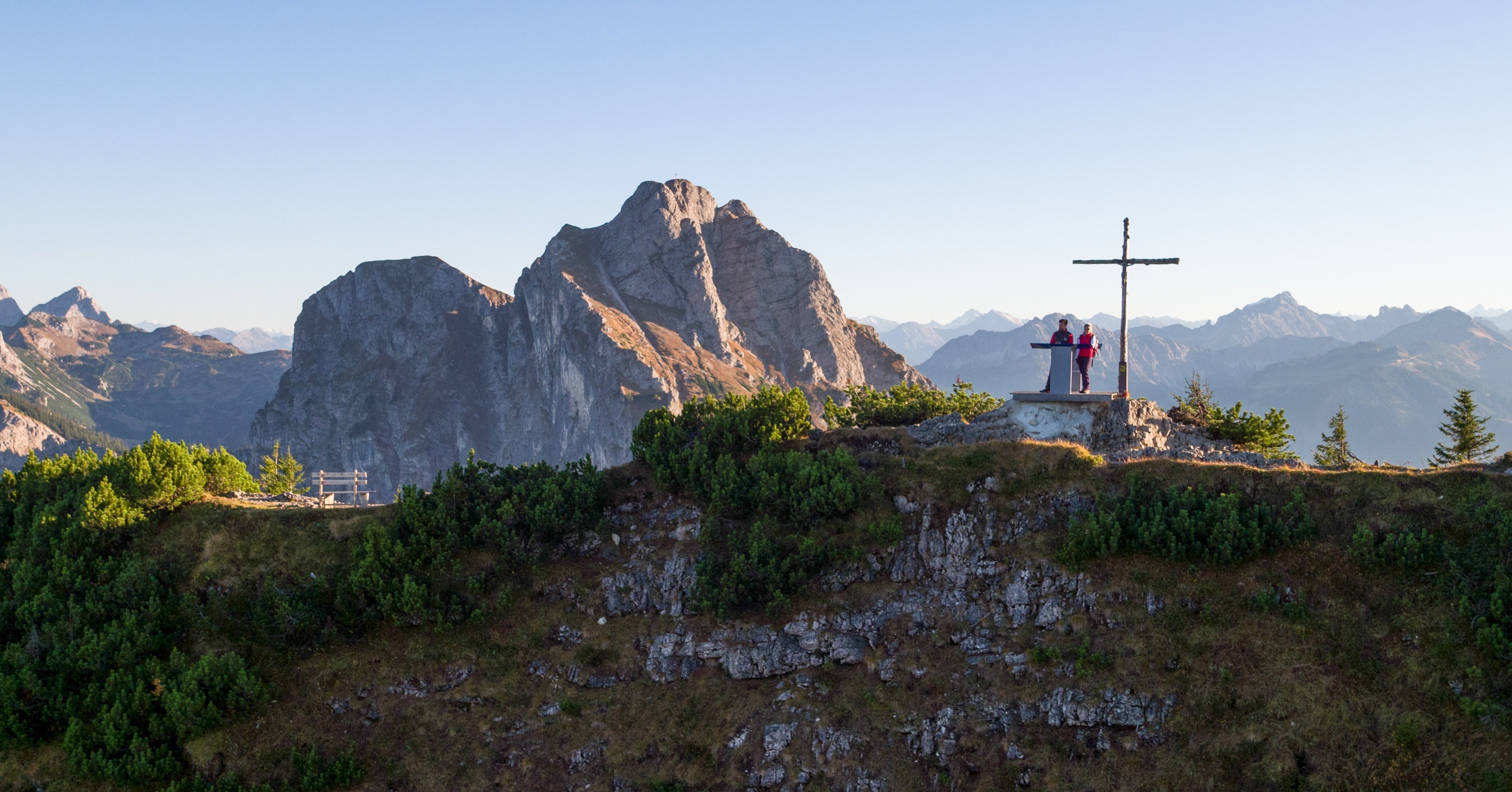 Wanderer stehen am Gipfelkreuz auf dem Breitenberg vor einer tollen Bergkulisse.
