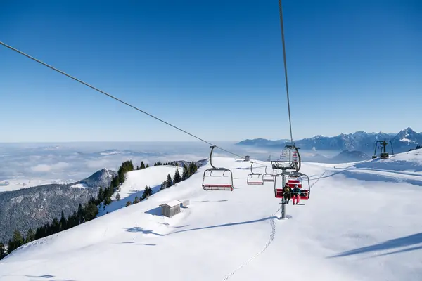 Blick von der Sesselbahn am Breitenberg über eine idyllisch verschneite Winterlandschaft mit den Allgäuer Bergen im Hintergrund.