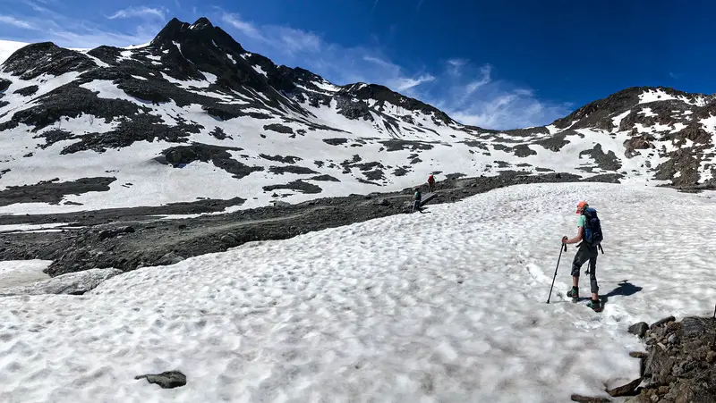 Wanderer in einer felsigen Berglandschaft, die teilweise von Schnee bedeckt ist.