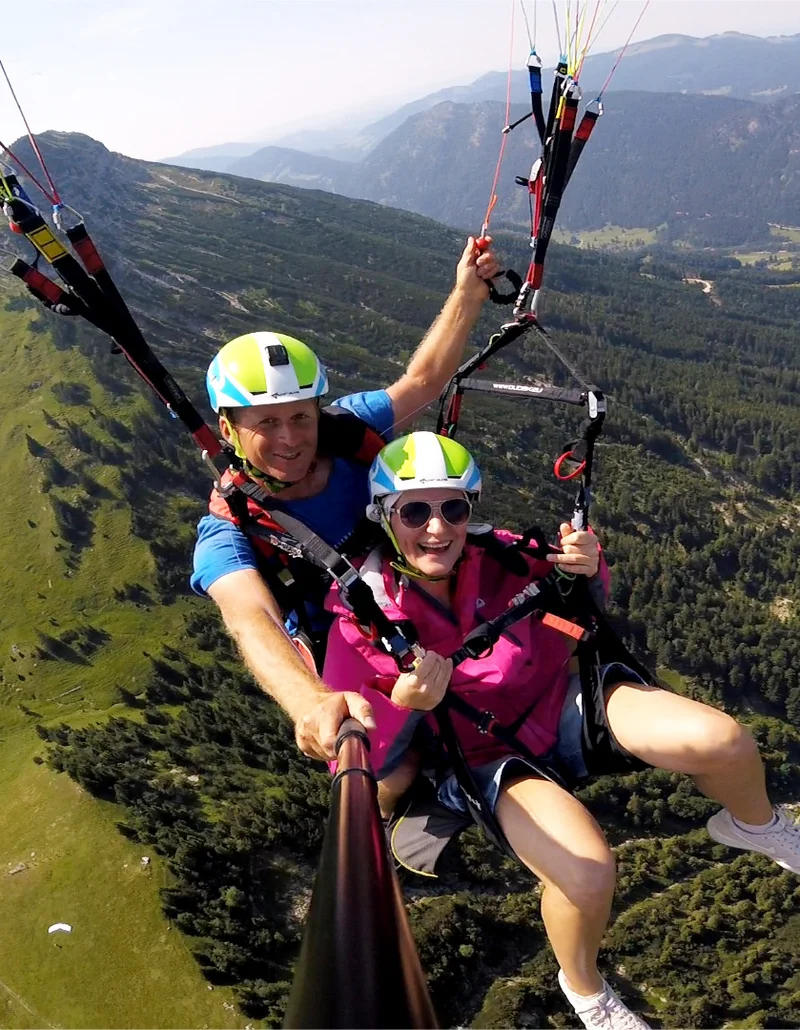 Ein Tandemflug mit dem Gleitschirm bei Sonnenschein und einer Aussicht auf eine schöne Berglandschaft.