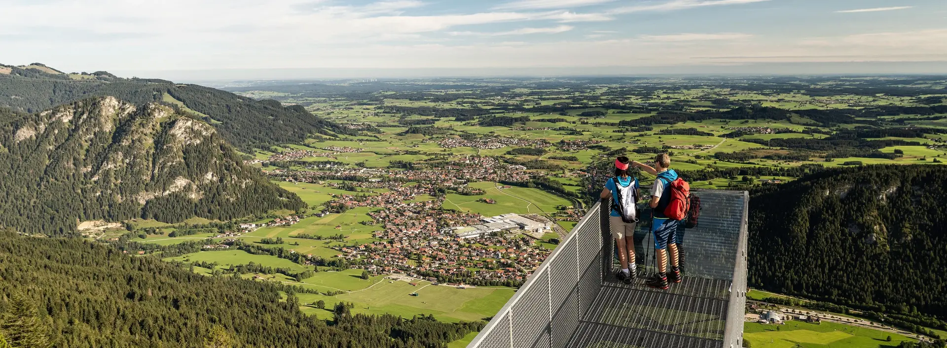 Weitreichender Blick über den Aussichtssteg auf dem Breitenberg auf das Pfrontener Tal und die umliegende Berglandschaft.