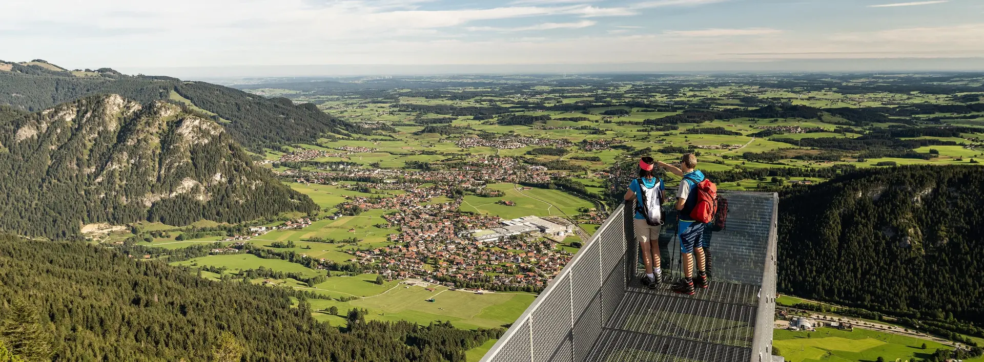 Weitreichender Blick über den Aussichtssteg auf dem Breitenberg auf das Pfrontener Tal und die umliegende Berglandschaft.