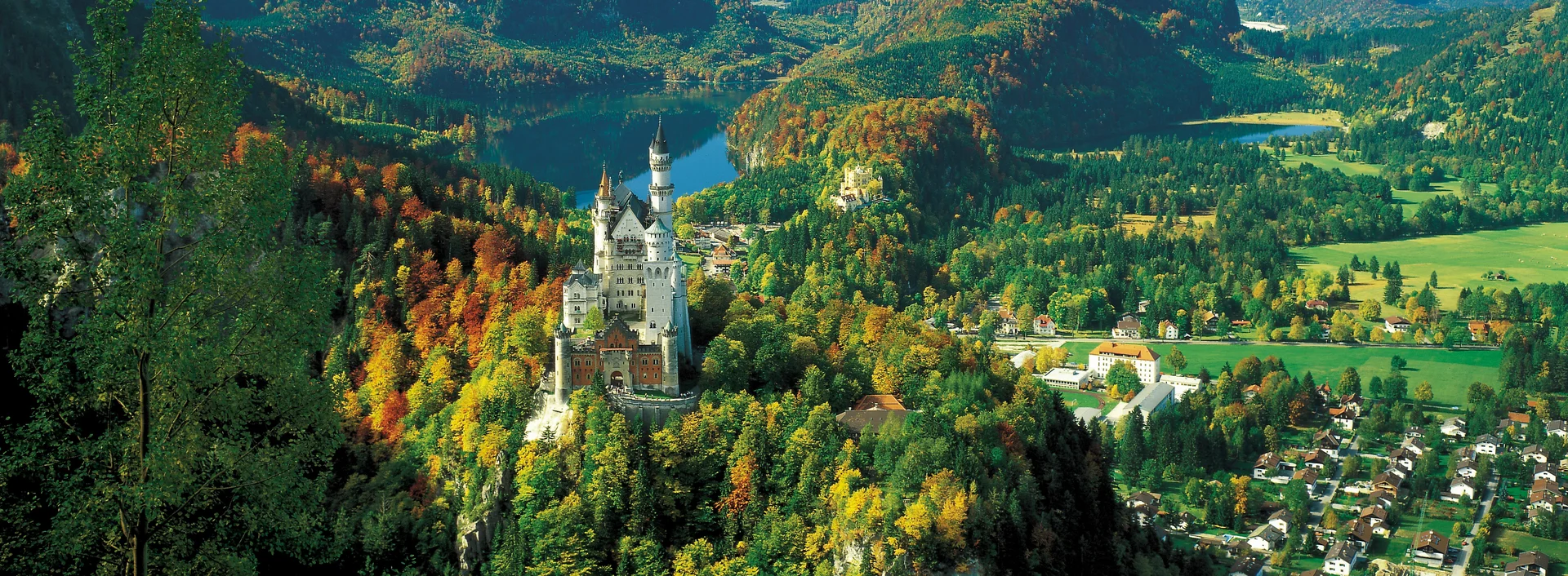 Panoramablick auf das Schloss Neuschwanstein im Allgäu und die umliegende Bergkulisse.