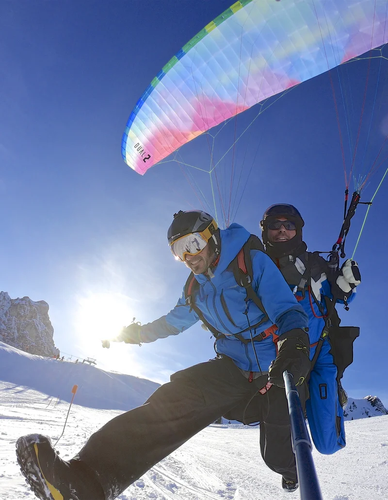 Ein Tandemflug mit dem Gleitschirm bei Sonnenschein und einer winterlichen Schneelandschaft.