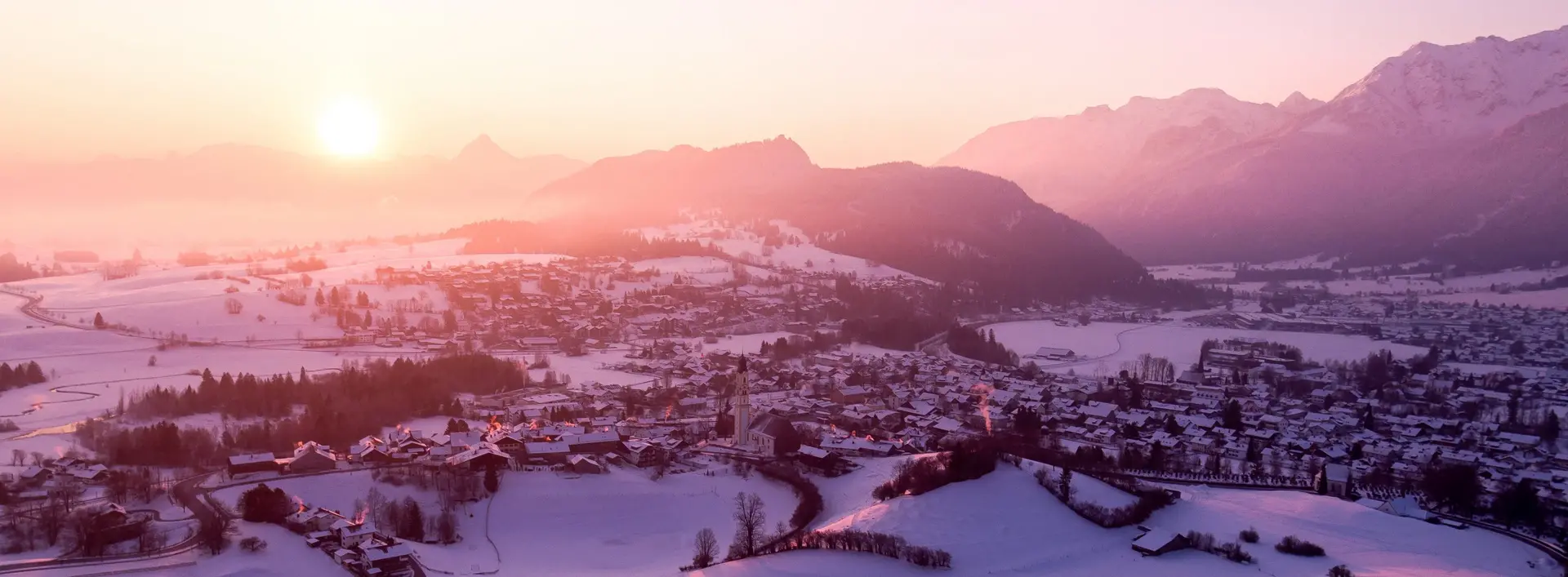 Malerischer Panoramablick auf das idyllisch verschneite Pfrontener Tal bei einem magischen Farbenspiel der Sonne.