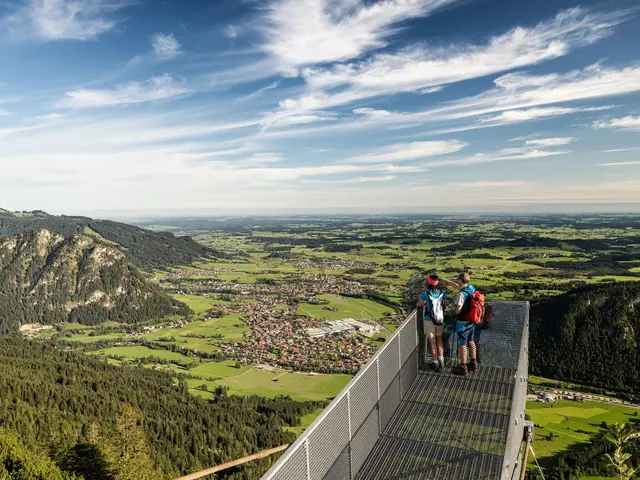 Zwei Wanderer auf dem Aussichtssteg am Breitenberg mit weitem Blick in das Pfrontener Tal.