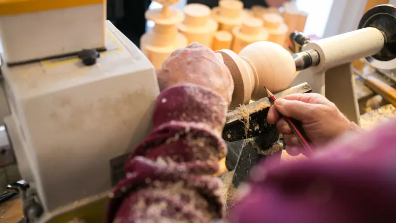 Mit verschiedenen Werkzeugen wird ein Werkstück aus Holz bearbeitet.