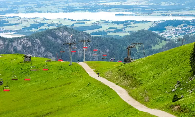 Mountainbiker fahren einen schmalen Weg bergab durch die Allgäuer Berglandschaft mit Blick in das Pfrontener Tal.