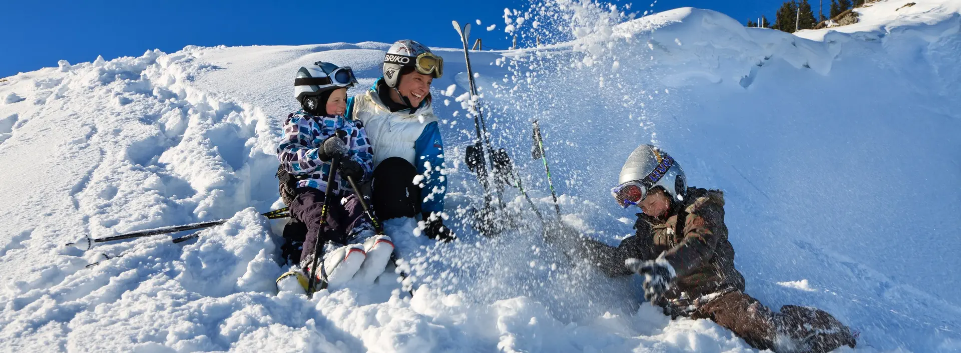 Wintervergnügen mit der ganzen Familie in Pfronten im Allgäu Eine Skifahrerfamilie sitzt bei sonnigem Wetter im Schnee und hat Spaß.