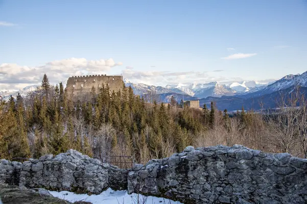 Blick auf eine imposante Burgruine mit einer winterlichen Bergkulisse im Hintergrund.