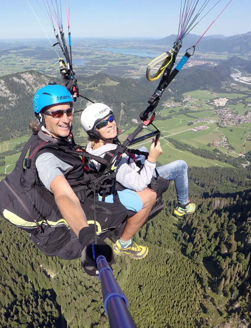 Ein Tandemflug mit dem Gleitschirm bei Sonnenschein und einer Aussicht auf eine schöne Berglandschaft.