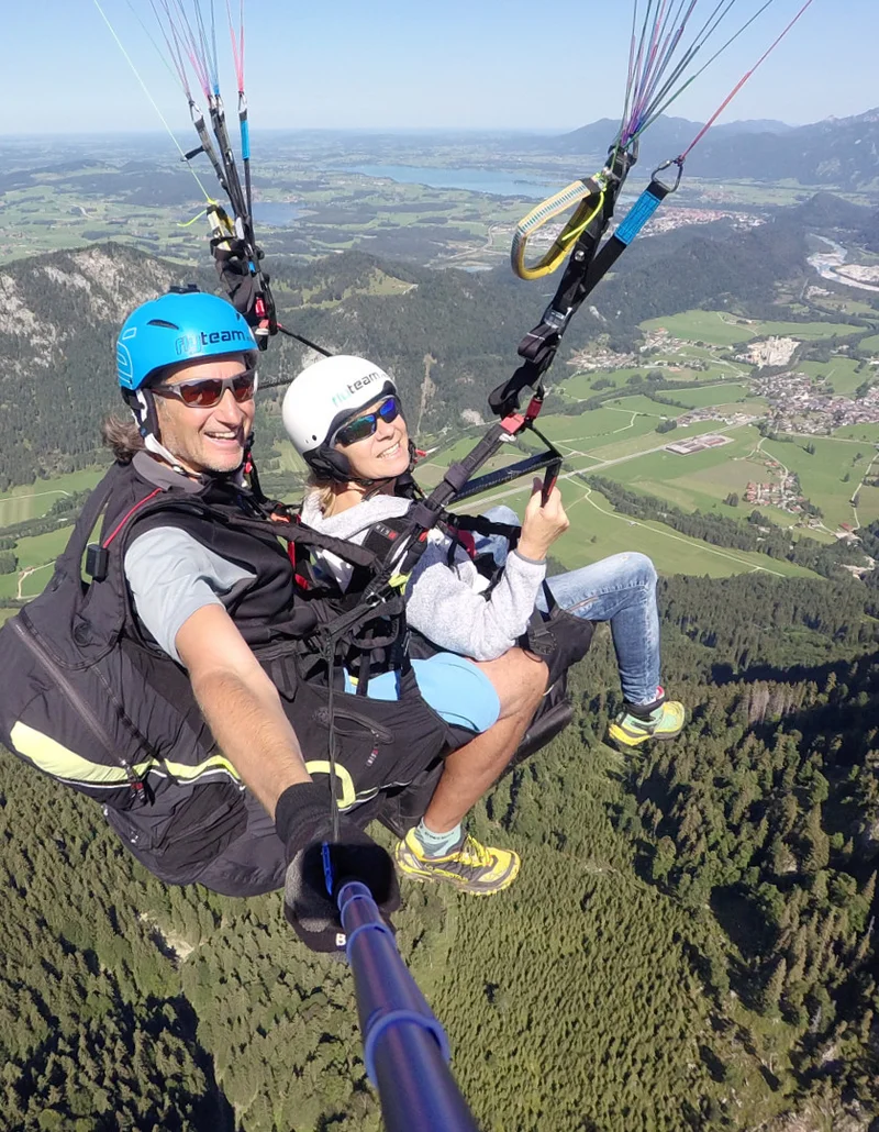 Ein Tandemflug mit dem Gleitschirm bei Sonnenschein und einer Aussicht auf eine schöne Berglandschaft.
