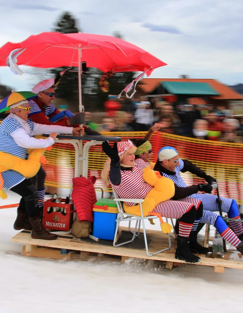 Mehrere Personen auf einem selbstgebauten Schlitten beim Gaudirennen in Pfronten im Allgäu.