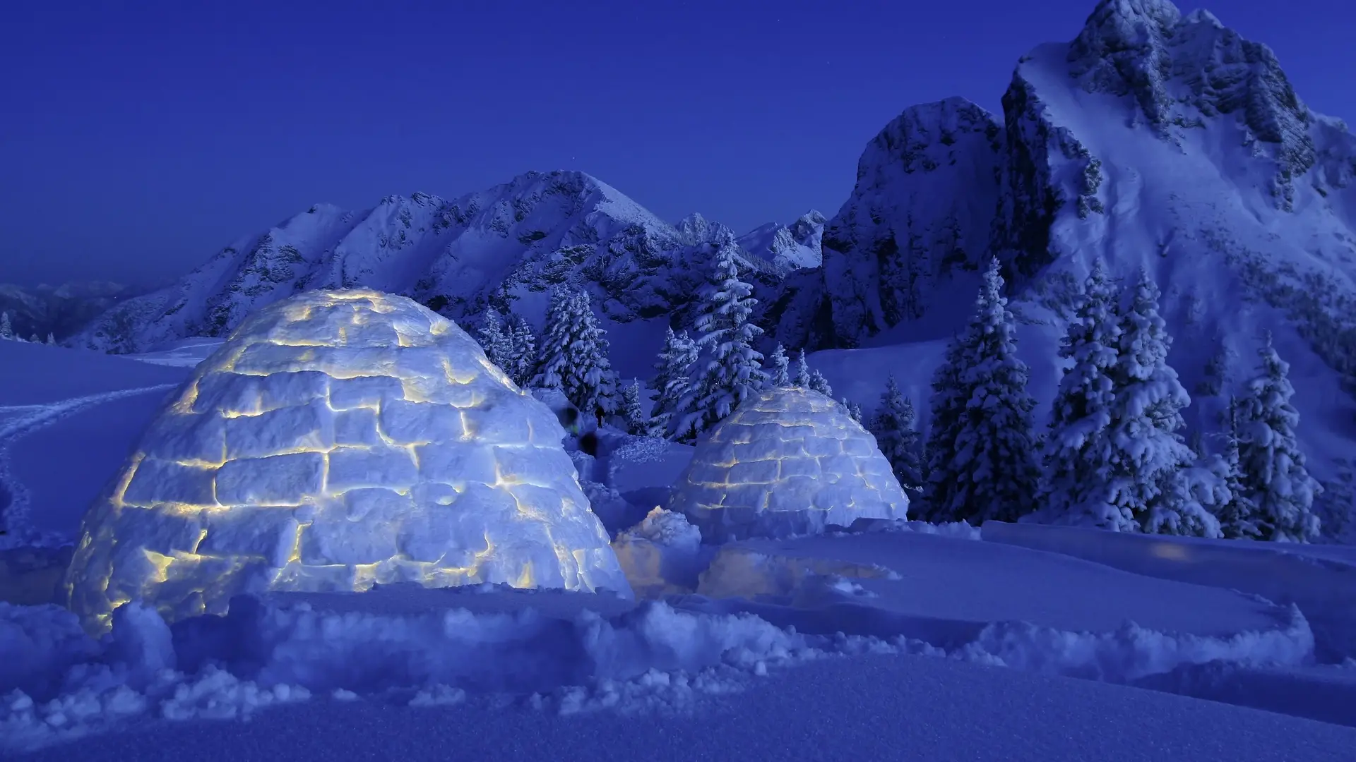 Übernachtungsmöglichkeit in einem selbstgebauten Iglu bei Dunkelheit mit Bergkulisse.