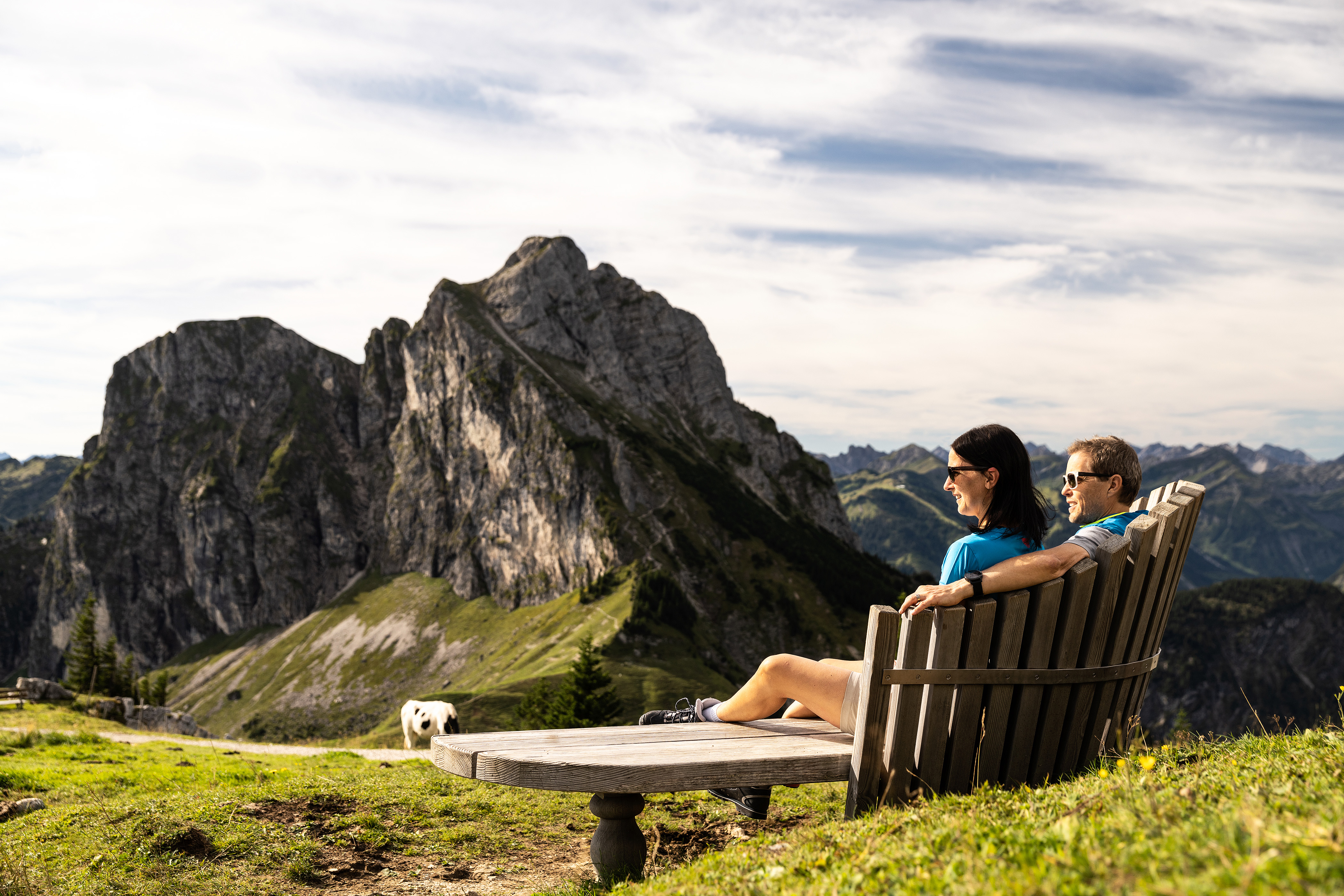 Zwei Wanderer auf einer Sitzbank mit Blick auf die beeindruckende Bergkulisse.